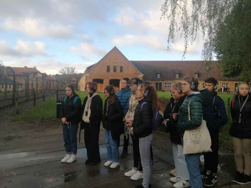 Uczniowie klasy 8 stoją przed bramą z napisem „Arbeit macht frei”